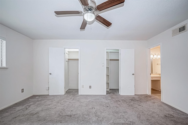 unfurnished bedroom featuring visible vents, connected bathroom, light colored carpet, ceiling fan, and multiple closets