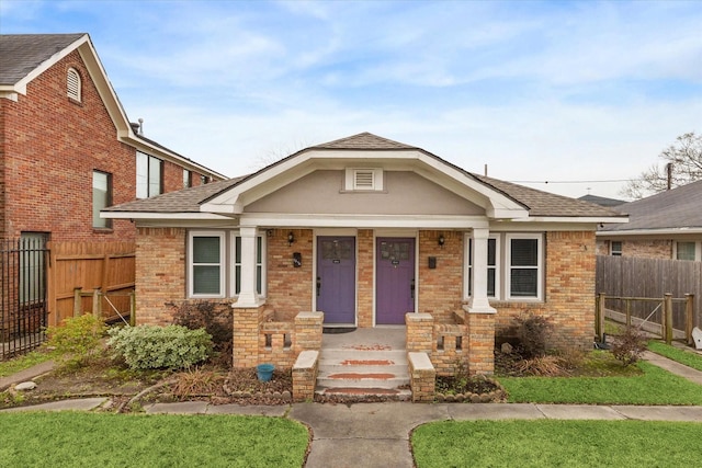 bungalow with covered porch, brick siding, fence, and roof with shingles