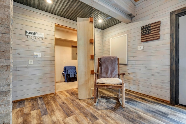 living area with electric panel, beamed ceiling, wooden walls, and wood finished floors