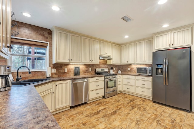 kitchen with stainless steel appliances, visible vents, cream cabinets, a sink, and under cabinet range hood