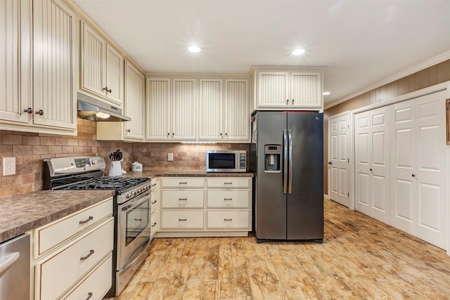 kitchen with decorative backsplash, dark countertops, appliances with stainless steel finishes, cream cabinetry, and under cabinet range hood