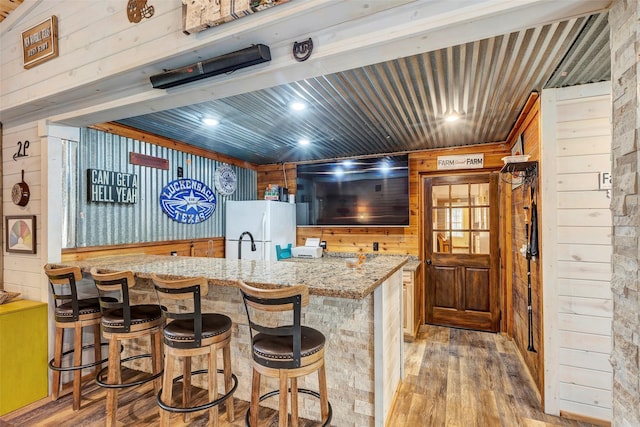 kitchen featuring wooden walls, light wood-style flooring, a kitchen breakfast bar, freestanding refrigerator, and light stone countertops