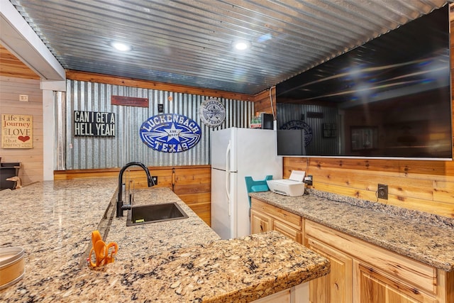 kitchen featuring light brown cabinets, wood walls, a sink, and freestanding refrigerator