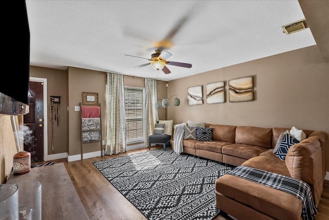 living area with ceiling fan, wood finished floors, visible vents, and baseboards