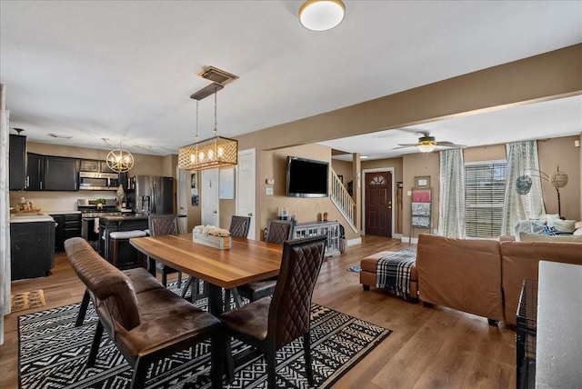 dining area featuring visible vents, baseboards, light wood-style flooring, stairway, and ceiling fan with notable chandelier