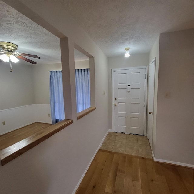 doorway to outside with light wood-style flooring, baseboards, ceiling fan, and a textured ceiling