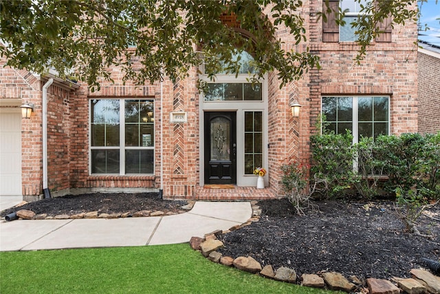 view of exterior entry with a garage, brick siding, and a lawn