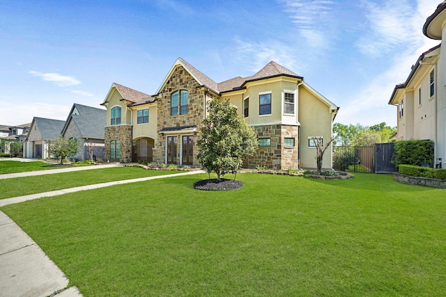 french country home featuring stone siding, fence, a front lawn, and stucco siding