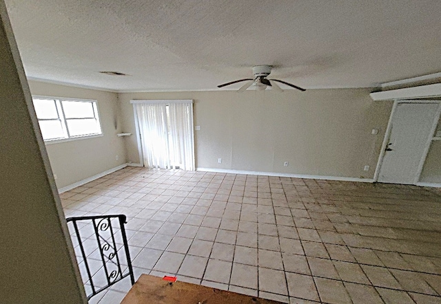 empty room with a textured ceiling, light tile patterned floors, a ceiling fan, and baseboards