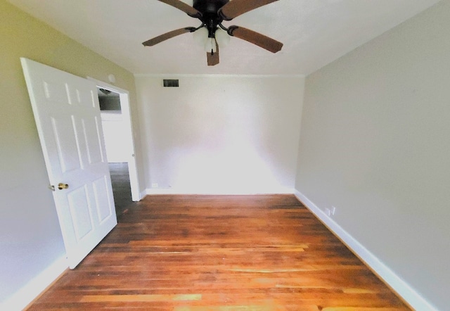 empty room with dark wood-style flooring, visible vents, and baseboards