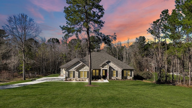 view of front of house featuring a forest view, stone siding, and a yard