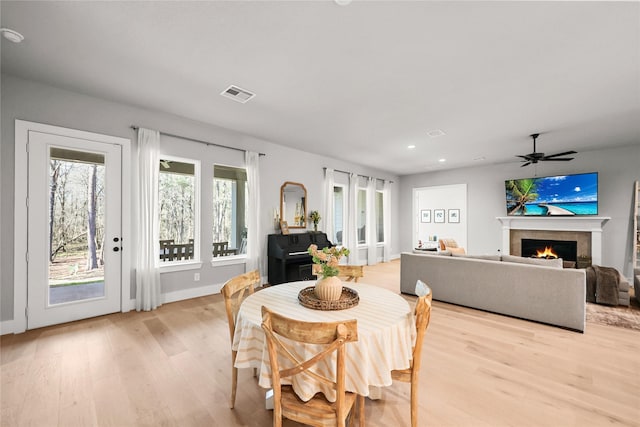 dining room with a warm lit fireplace, visible vents, ceiling fan, light wood-style floors, and recessed lighting