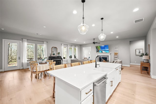 kitchen with a warm lit fireplace, visible vents, open floor plan, light wood-type flooring, and stainless steel dishwasher