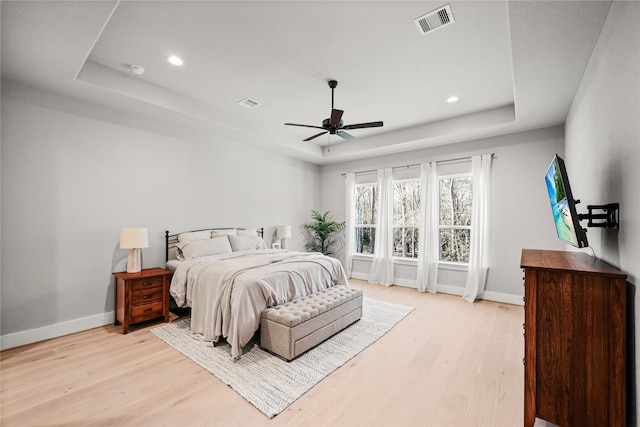 bedroom with light wood-type flooring, a tray ceiling, visible vents, and baseboards