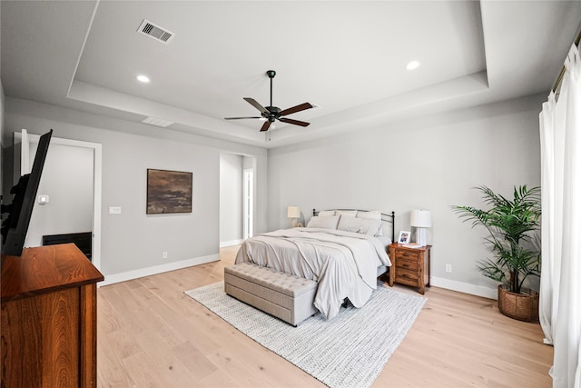 bedroom with a tray ceiling, light wood-style flooring, visible vents, and baseboards