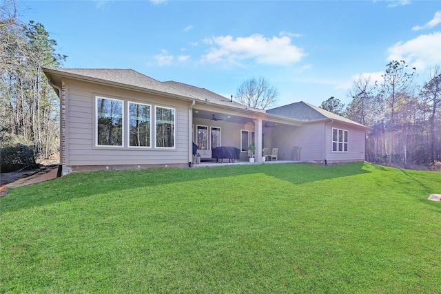 rear view of property featuring a patio, a shingled roof, a lawn, and a ceiling fan