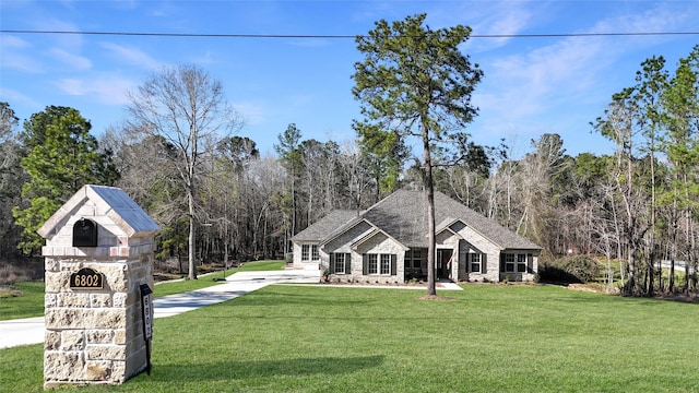 exterior space with stone siding, a front yard, concrete driveway, and a forest view