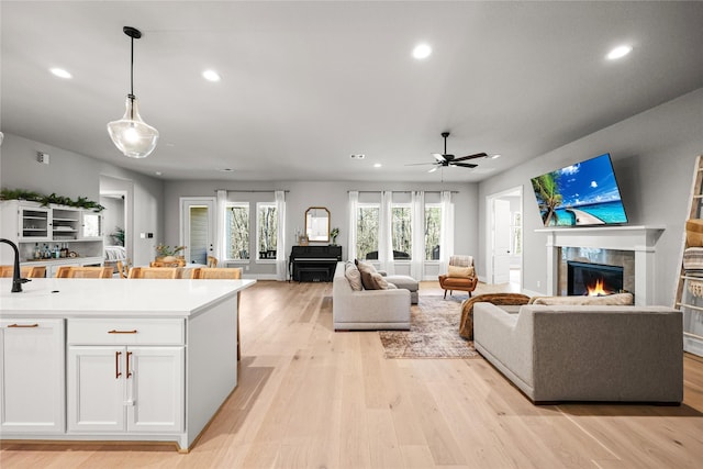 living area featuring a warm lit fireplace, light wood finished floors, a ceiling fan, and recessed lighting