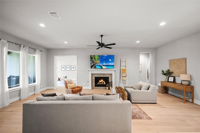 living area featuring a lit fireplace, light wood-style flooring, visible vents, and recessed lighting