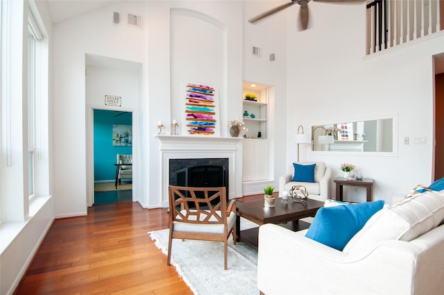 living room with visible vents, ceiling fan, built in features, a fireplace, and wood finished floors