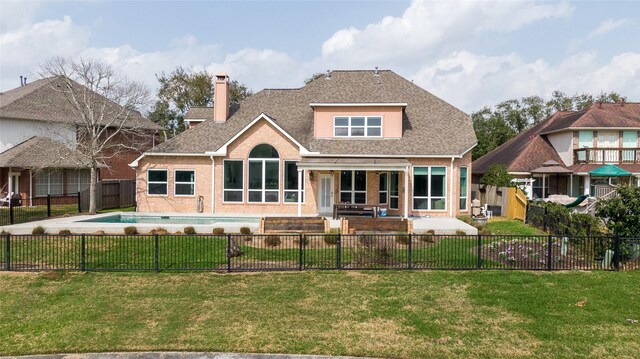 rear view of property featuring a fenced backyard, a yard, a fenced in pool, brick siding, and a patio area