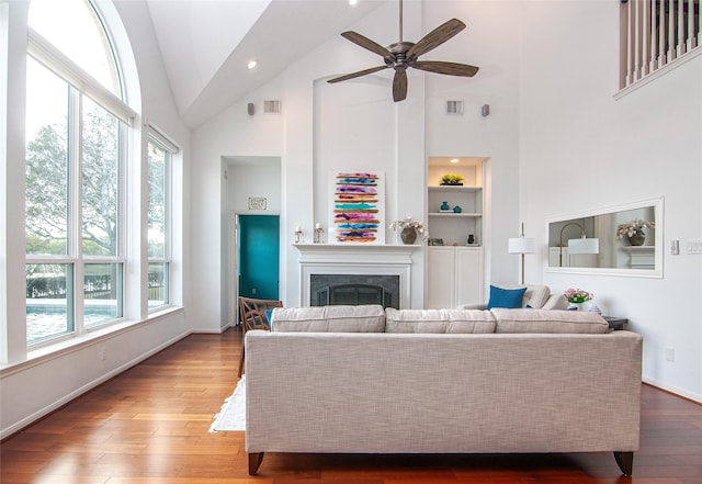 living area featuring visible vents, built in shelves, high vaulted ceiling, wood finished floors, and a fireplace