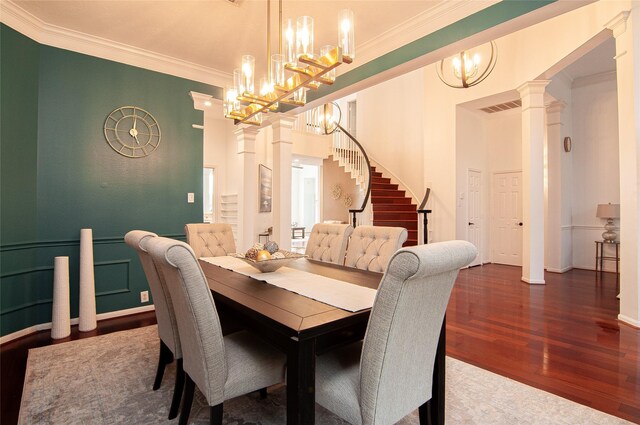 dining room with wood finished floors, visible vents, decorative columns, ornamental molding, and stairs