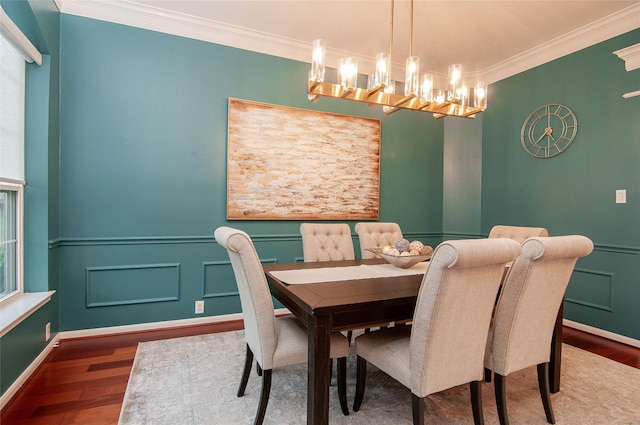 dining area featuring crown molding, a decorative wall, wood finished floors, and wainscoting