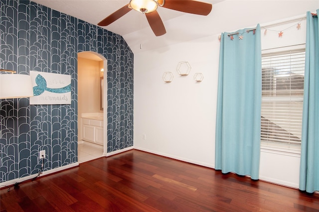 empty room with lofted ceiling, a ceiling fan, wood finished floors, wallpapered walls, and baseboards