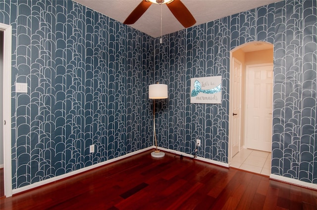 spare room with wood finished floors, wallpapered walls, arched walkways, ceiling fan, and a textured ceiling