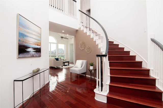 stairs with a ceiling fan, a high ceiling, wood finished floors, and baseboards