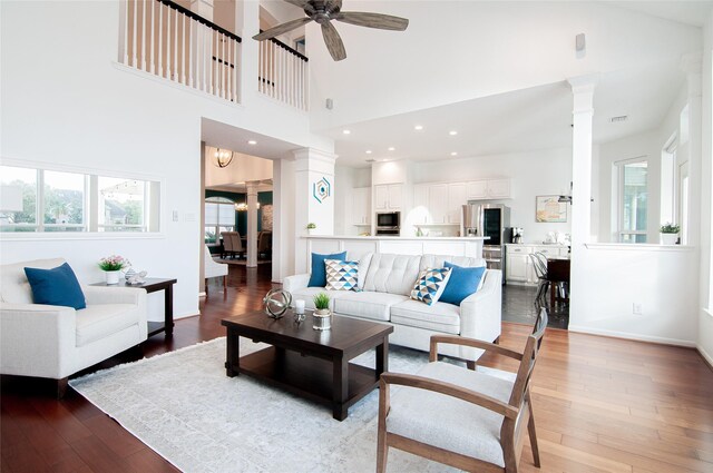 living room featuring ceiling fan, baseboards, light wood-style flooring, and ornate columns