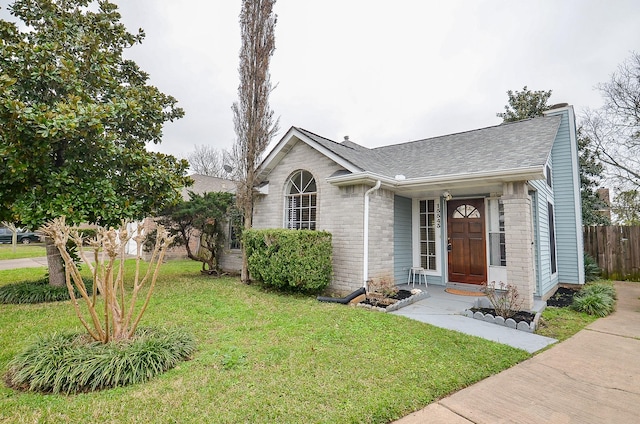 view of front of home featuring a front lawn, a shingled roof, fence, and brick siding