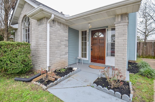 view of exterior entry with brick siding and fence