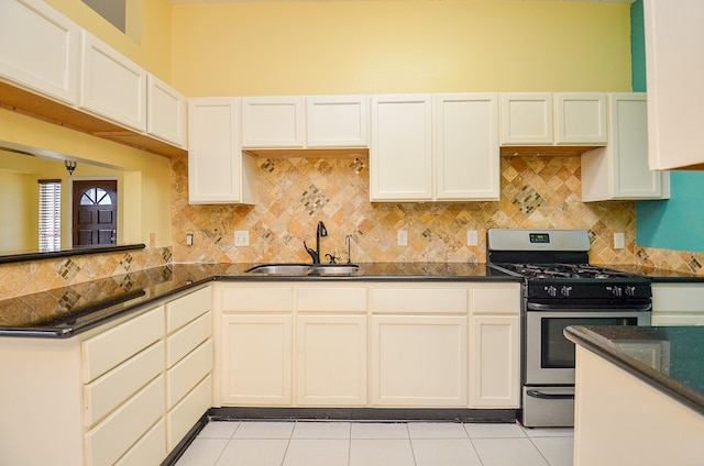 kitchen with tasteful backsplash, dark stone counters, stainless steel range with gas stovetop, a sink, and light tile patterned flooring