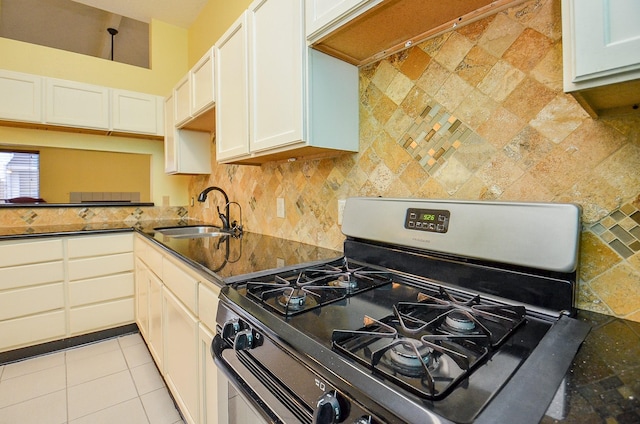 kitchen featuring light tile patterned floors, tasteful backsplash, white cabinets, stainless steel gas stove, and a sink