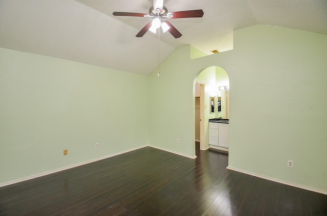 spare room featuring baseboards, arched walkways, ceiling fan, dark wood-style flooring, and vaulted ceiling