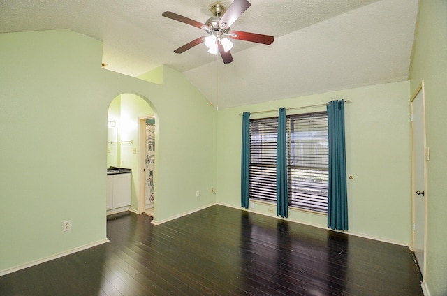 empty room featuring lofted ceiling, arched walkways, a ceiling fan, baseboards, and dark wood finished floors