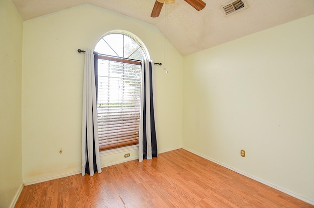 spare room featuring light wood finished floors, lofted ceiling, visible vents, a ceiling fan, and baseboards