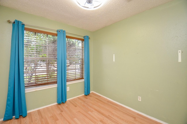 spare room featuring a textured ceiling, light wood-style flooring, and baseboards