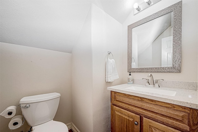 half bathroom featuring toilet, vaulted ceiling, and vanity