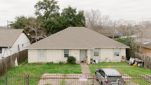 view of front facade with brick siding, a front lawn, a shingled roof, and fence private yard