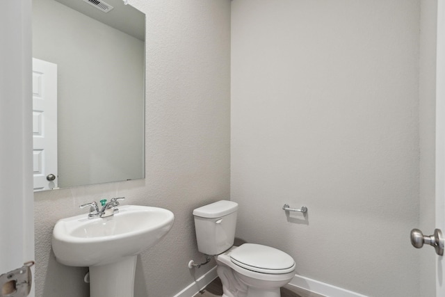 half bathroom featuring visible vents, a sink, toilet, and baseboards