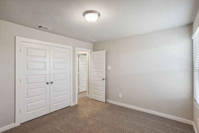 unfurnished bedroom featuring a closet, visible vents, carpet flooring, a textured ceiling, and baseboards