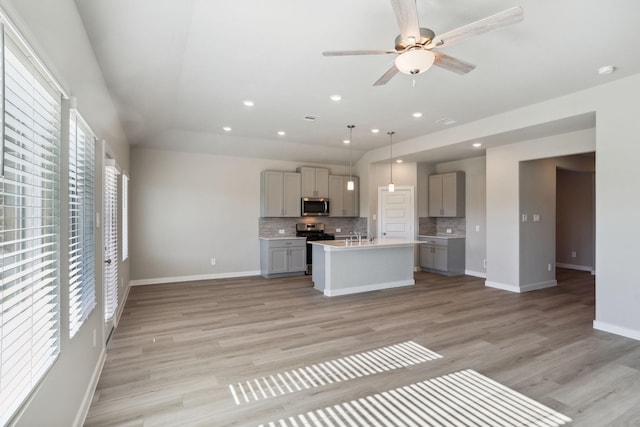 kitchen featuring a center island with sink, hanging light fixtures, stainless steel appliances, gray cabinets, and light countertops