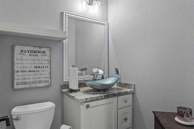 bathroom featuring toilet, a textured wall, and vanity