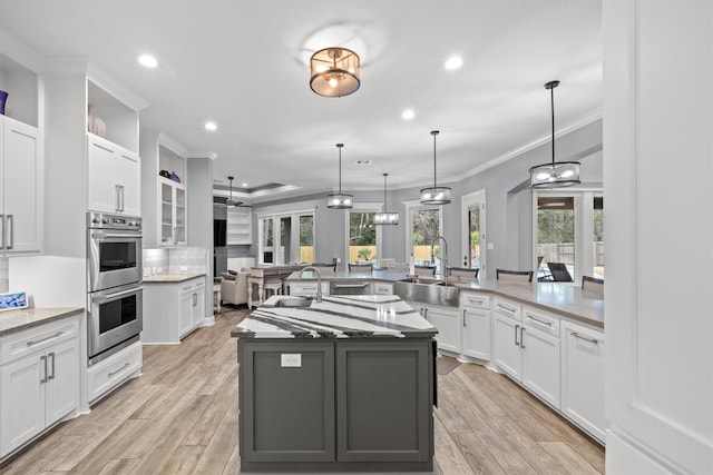 kitchen featuring double oven, a sink, white cabinets, a large island, and pendant lighting