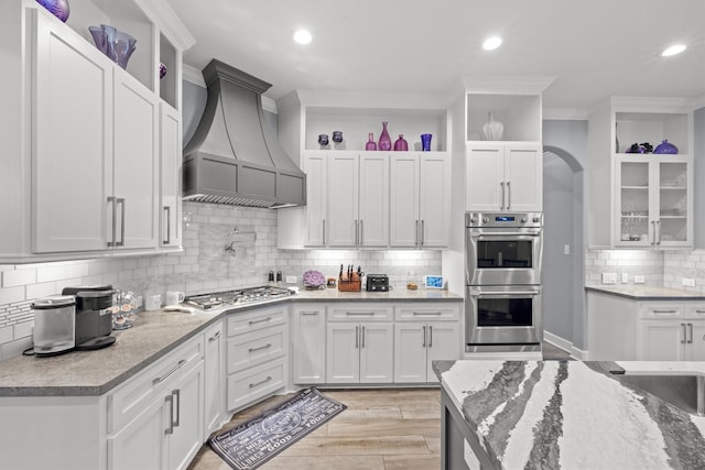 kitchen featuring white cabinets, glass insert cabinets, custom exhaust hood, stainless steel appliances, and open shelves