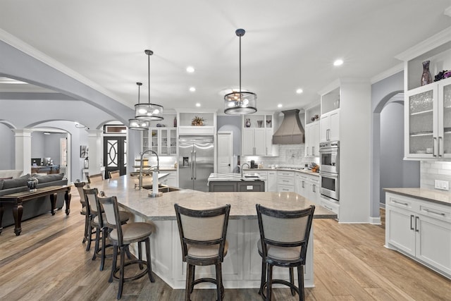 kitchen with glass insert cabinets, arched walkways, stainless steel appliances, and a spacious island