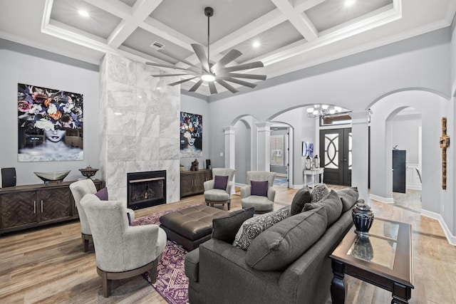 living room featuring arched walkways, a high ceiling, a tiled fireplace, wood finished floors, and ornate columns